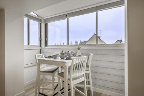 une table et des chaises blanches dans une chambre avec fenêtres dans l'établissement Douceur et tranquillité sur la Presqu'Île de Rhuys, à Sarzeau