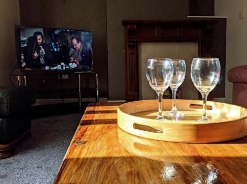 two wine glasses on a wooden table in front of a tv at Racecourse Cottage in Doncaster