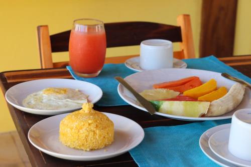 a table with plates of food and a glass of juice at Pousada Ventos do Guajiru-Casa de Kitesurfistas in Itarema