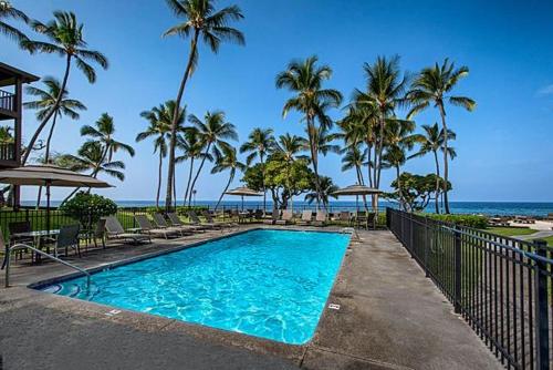 a swimming pool with chairs and palm trees and the ocean at Kona Isle E23 in Kailua-Kona