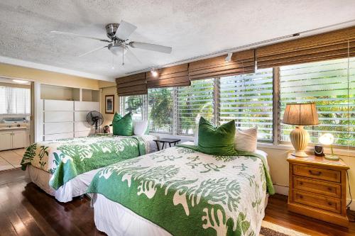 a bedroom with two beds with green comforters and a window at Hale Pahukoa in Kailua-Kona