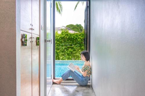 a woman sitting in a doorway reading a book at Book a Bed Poshtel - SHA Plus in Phuket Town