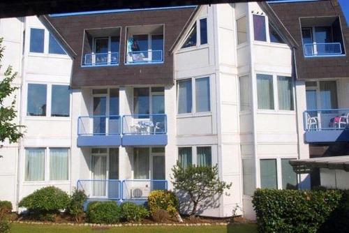 een wit appartementencomplex met blauwe balkons en struiken bij Appartement 1 Haus Residenz in Sankt Peter-Ording