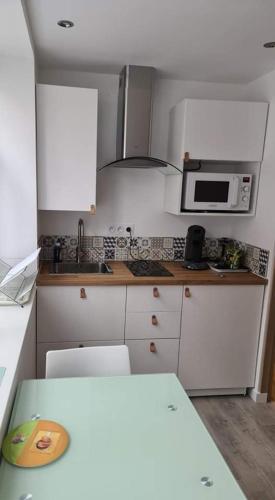 - une cuisine avec des placards blancs, un four micro-ondes et une table dans l'établissement Studio L'orée du port, à Saint-Valery-en-Caux