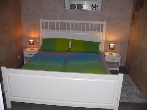 uma cama branca com 2 almofadas verdes e 2 candeeiros em Ferienwohnung Natur-Pur em Ehrenberg