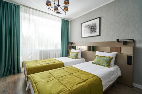 two beds in a hotel room with green curtains at Ugor Hotel in Syktyvkar