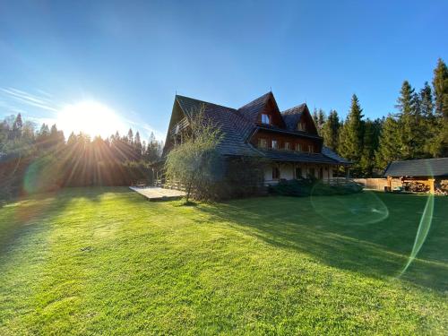 a large house on a grassy yard with the sun in the background at Willa Arnika in Lutowiska