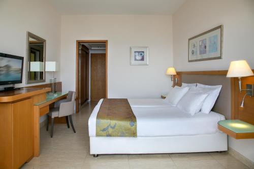 a hotel room with a bed and a desk and a television at Atlantica Miramare Beach in Limassol