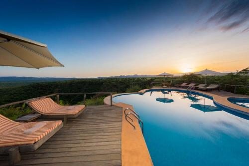 a swimming pool with chairs and an umbrella at Escarpment Luxury Lodge Manyara in Mto wa Mbu