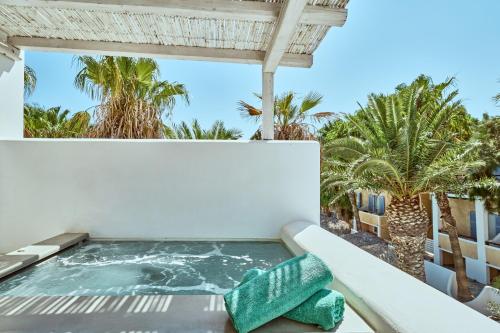 a hot tub on the balcony of a resort with palm trees at Meltemi Excelsior Suites in Perissa
