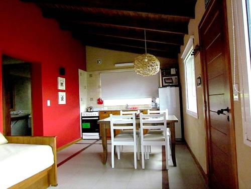cocina con mesa, sillas blancas y paredes rojas en Las Calandrias de Tandil en Tandil