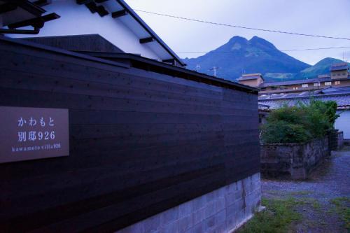 a brick wall with a sign on it with mountains in the background at かわもと別邸９２６ in Yufuin
