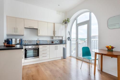 a kitchen with white cabinets and a table and a blue chair at Bells Chapel - Bright Rooftop Apartment in the Centre of Town with Juliet Balconies in Falmouth