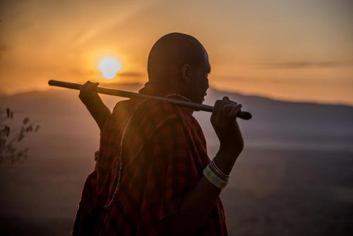 a man holding a stick in front of the sunset at Escarpment Luxury Lodge Manyara in Mto wa Mbu