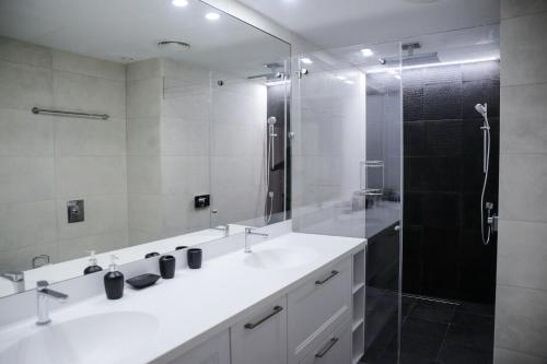 a bathroom with two sinks and a shower with a glass door at YalaRent Midtown towers TLV in Tel Aviv