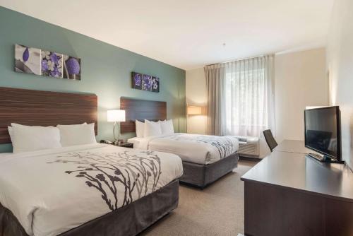 a hotel room with two beds and a flat screen tv at Sleep Inn & Suites at Kennesaw State University in Kennesaw