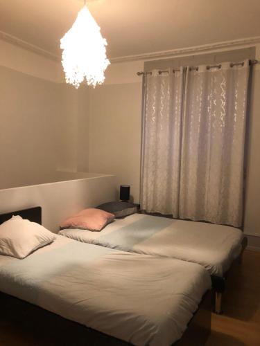 2 Betten in einem Zimmer mit einem Fenster und einem Kronleuchter in der Unterkunft LE BRETZEL in Colmar