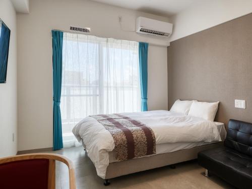 a bedroom with a bed and a chair and a window at BiBi Hotel NAHA KUME in Naha