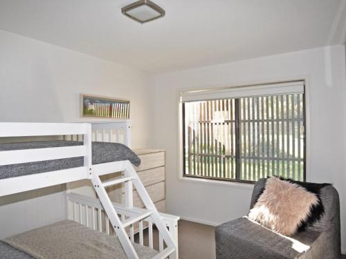 a bedroom with a bunk bed and a chair and a window at 52 ON BAYVIEW - PET FRIENDLY (OUTSIDE ONLY) in Inverloch