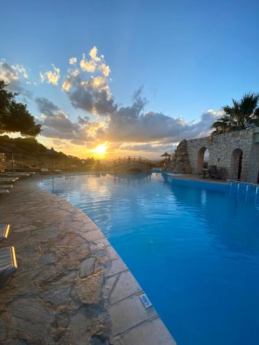 a large swimming pool with a sunset in the background at Arolithos Traditional Village Hotel in Tílisos
