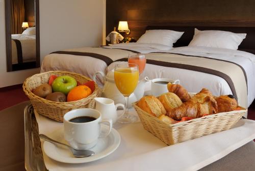 a breakfast table with baskets of bread and fruit on a bed at Golden Tulip Hotel de’ Medici in Bruges
