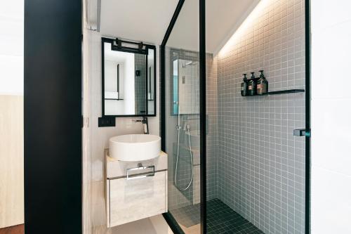 uma casa de banho com um lavatório e uma cabina de duche em vidro. em KēSa House, The Unlimited Collection managed by The Ascott Limited em Singapura