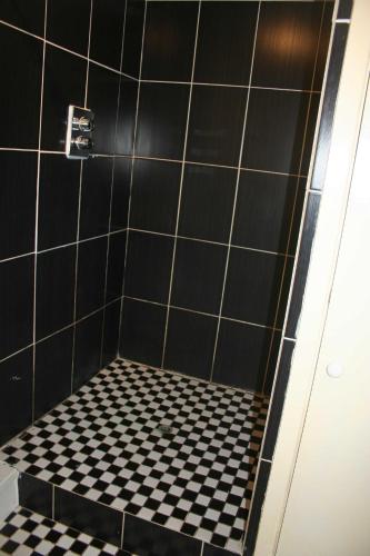 a black tiled shower with a black and white checkered floor at The Nook - Farm Park Stay with Hot Tub & Dome in Swansea
