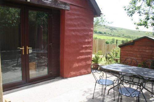 a patio with a table and chairs next to a red house at The Nook - Farm Park Stay with Hot Tub & Dome in Swansea
