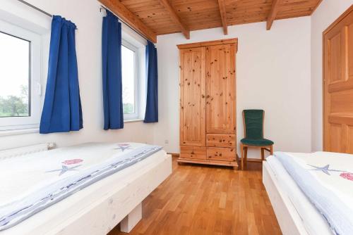 two beds in a bedroom with blue curtains and a chair at Ferienwohnungen im Haus Nordlichter in Holtgast