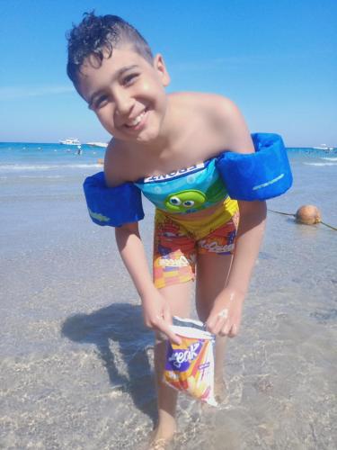 Ein kleiner Junge, der am Strand steht und eine Dose Chips hält. in der Unterkunft Chalets in Porto Sokhna Pyramids in Ain Suchna