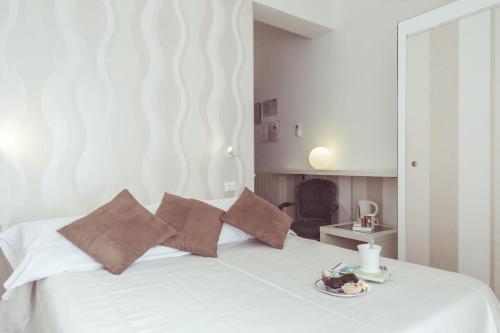 a white bed with pillows and a plate of food on it at Piccolo Mondo Hotel in Follonica