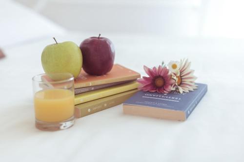 a glass of orange juice next to books with an apple and a bookinyl at Piccolo Mondo Hotel in Follonica