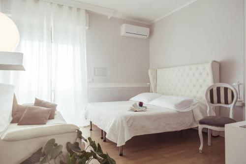 a white bedroom with two beds and a chair at Piccolo Mondo Hotel in Follonica