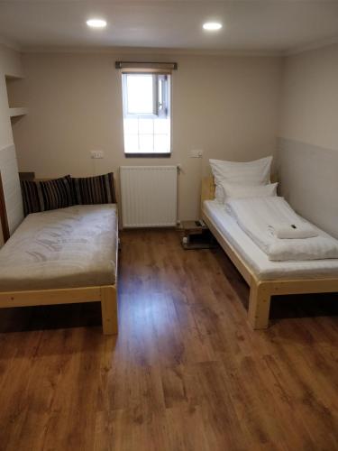 two beds in a room with wooden floors and a window at Dorottya Vendégház in Hódmezővásárhely