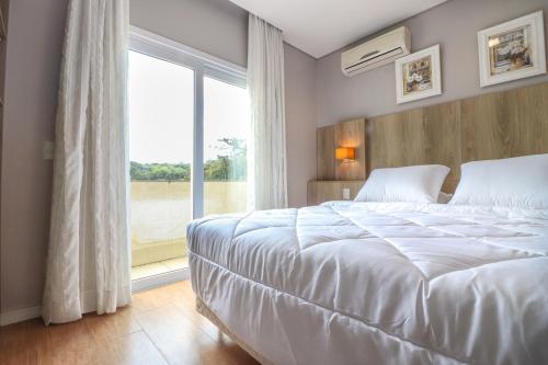 - une chambre avec un lit blanc et une grande fenêtre dans l'établissement Pousada Bella Viena, à Gramado