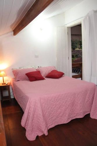 a pink bed with red pillows in a bedroom at Flat Vila da Arara in Maresias