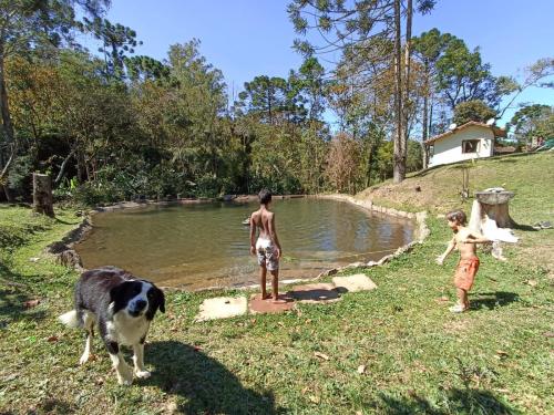 two children and a dog standing in front of a pond at Gran Camping Cabanas da Fazenda in Visconde De Maua