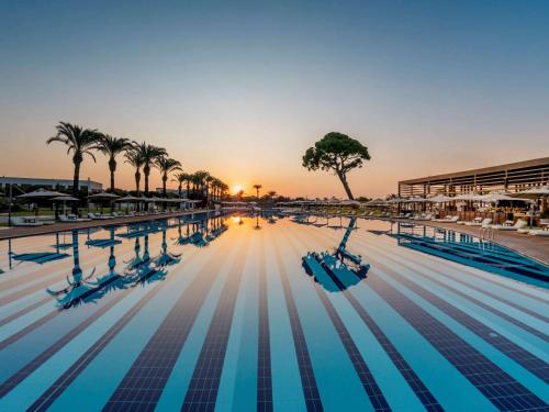 - une piscine avec des palmiers et le coucher du soleil dans l'établissement Rixos Premium Belek - The Land of Legends Access, à Belek