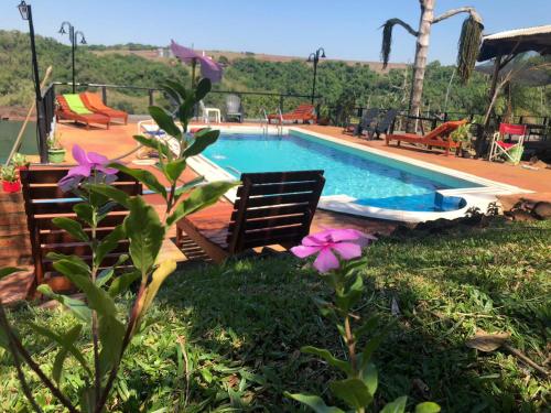 a swimming pool with two chairs and purple flowers at Stone Wall Cottages in Puerto Iguazú
