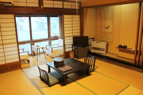 sala de estar con mesa, sillas y TV en Historical Ryokan SENYUKAN, en Ōwani