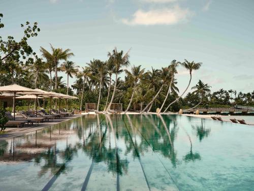 a pool at a resort with chairs and palm trees at Patina Maldives, Fari Islands in North Male Atoll