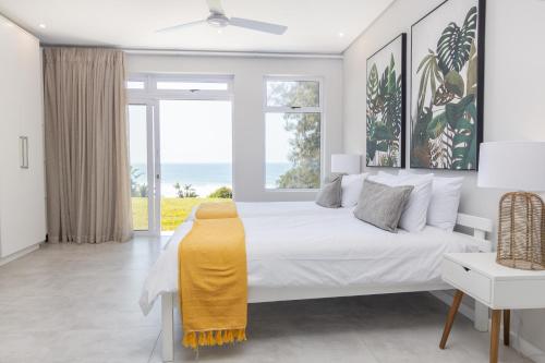 a white bedroom with a bed and a large window at NKWAZI COTTAGE, 77 Nkwazi Drive, Zinkwazi beach in Zinkwazi Beach