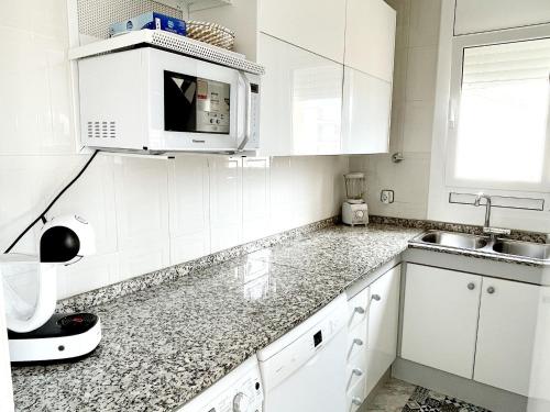 a white kitchen with white cabinets and a microwave at Open Sky, Apartamento con solárium privado y barbacoa in El Vendrell