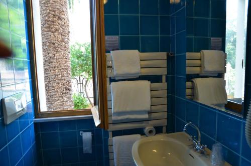 Baño de azulejos azules con lavabo y espejo en Hotel Villa Marina, en La Maddalena