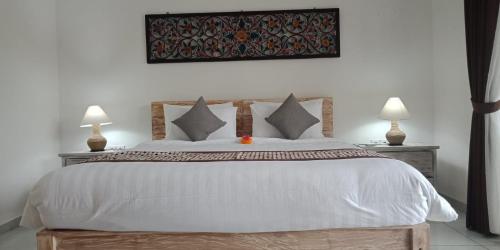 a bedroom with a large white bed with two lamps at Kapri Balinese House in Ubud