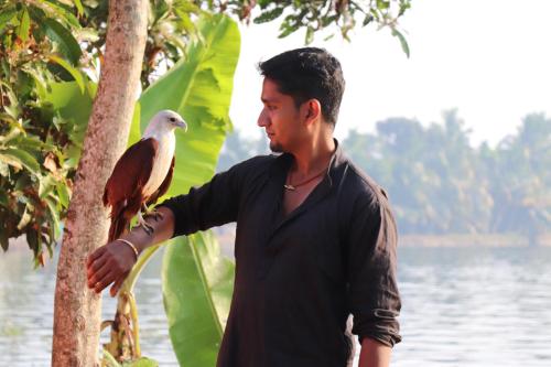 a man standing next to a tree with a bird on his arm at Marari houseboat in Mararikulam