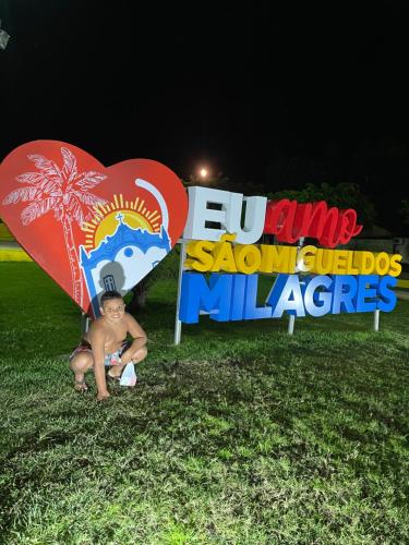a young boy sitting under a sign with a heart at Chalé Palhano Beach in São Miguel dos Milagres
