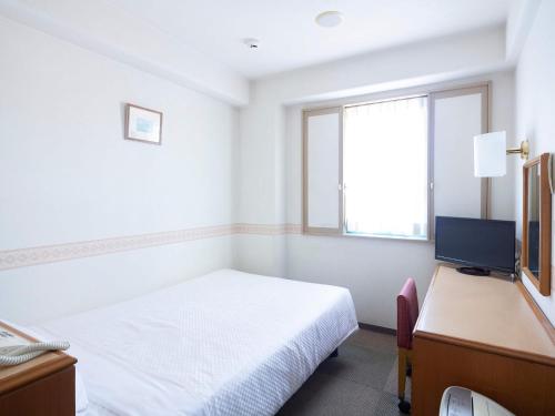 a white room with a bed and a television at Hotel Wing Port Nagasaki in Nagasaki