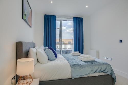 a bedroom with a bed with blue curtains and a window at Modern & Spacious Studio & One Bedroom Apartments in Heathrow in Hounslow