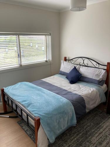 a bedroom with a bed with a blue blanket and two windows at Bruny Ocean Cottage in Alonnah